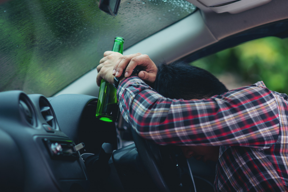 man holds a beer bottle while is driving a car