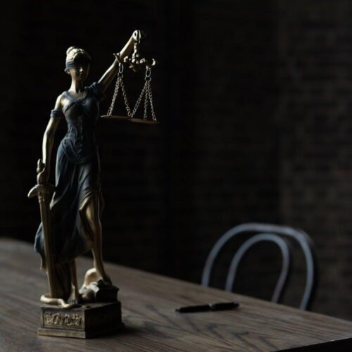 Free Lady Justice figurine on wooden table in dimly lit room symbolizes law and fairness. Stock Photo