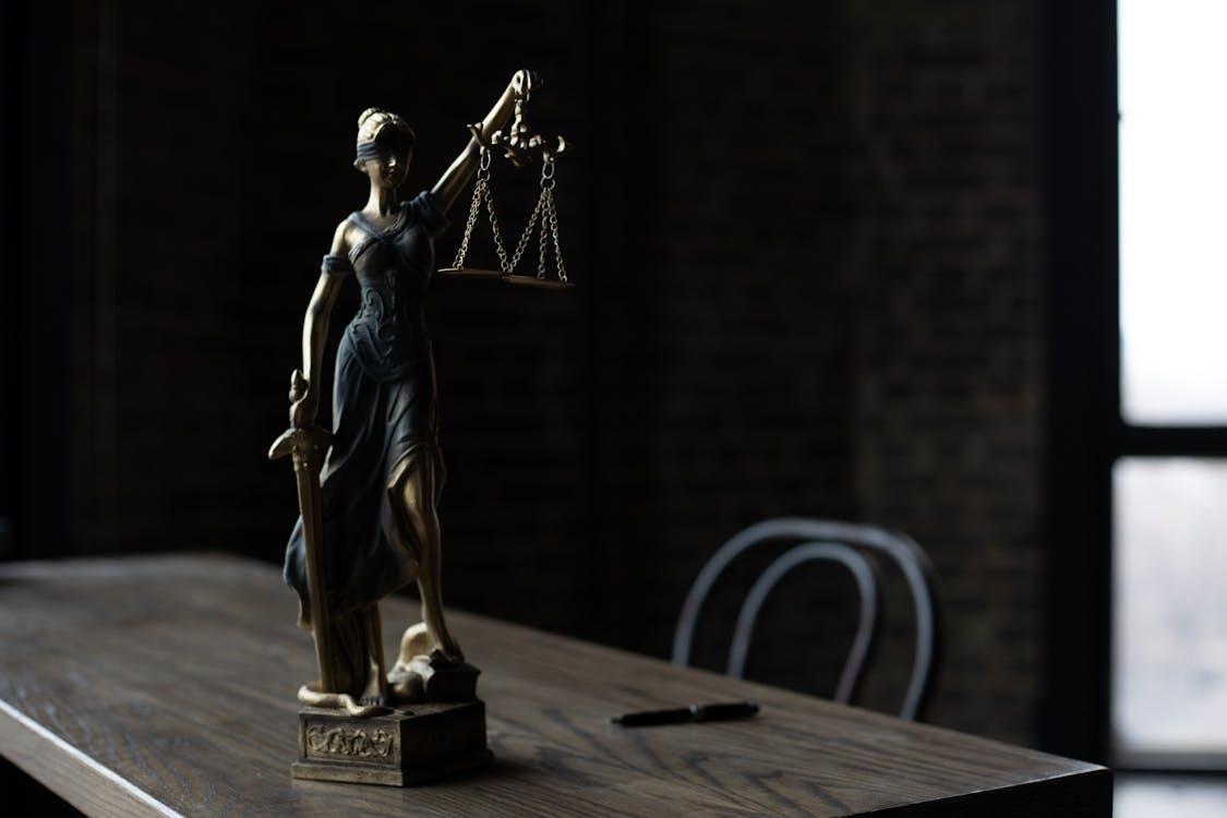Free Lady Justice figurine on wooden table in dimly lit room symbolizes law and fairness. Stock Photo