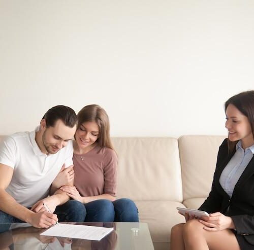couple smiling signing paper in front of a lawyer